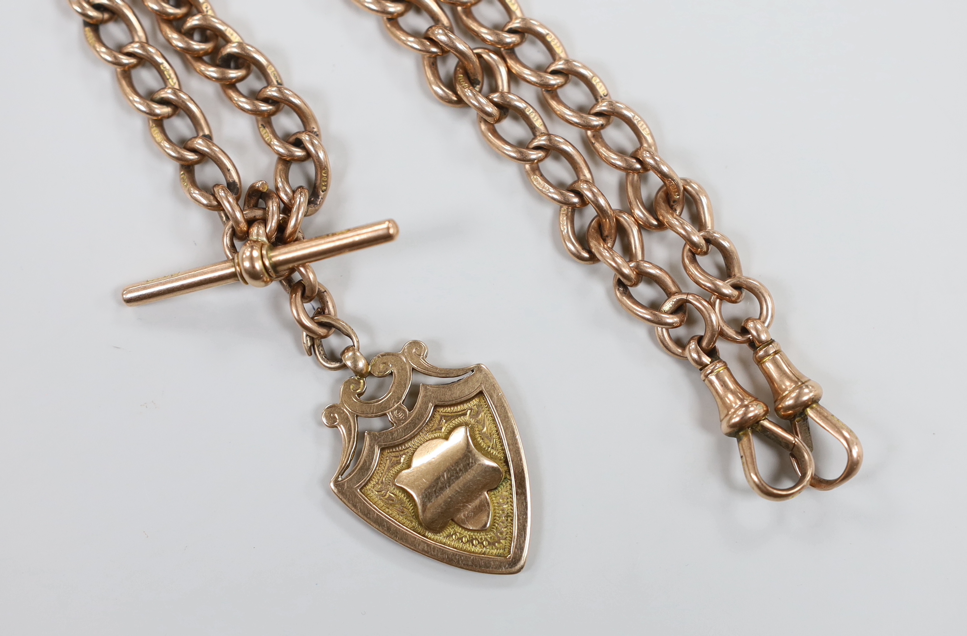 An early 20th century 9ct rose gold albert, 36cm, hung with a 9ct gold shield shaped medallion, 52.3 grams.